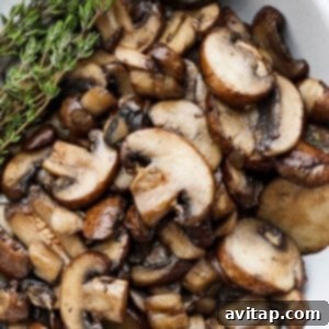 Roasted mushrooms in a white bowl with a sprig of thyme, ready to be served.