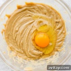 A bowl of tahini mixture with a raw egg, being mixed with a spatula.