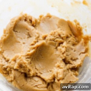 A glass bowl containing moldable tahini cookie dough.