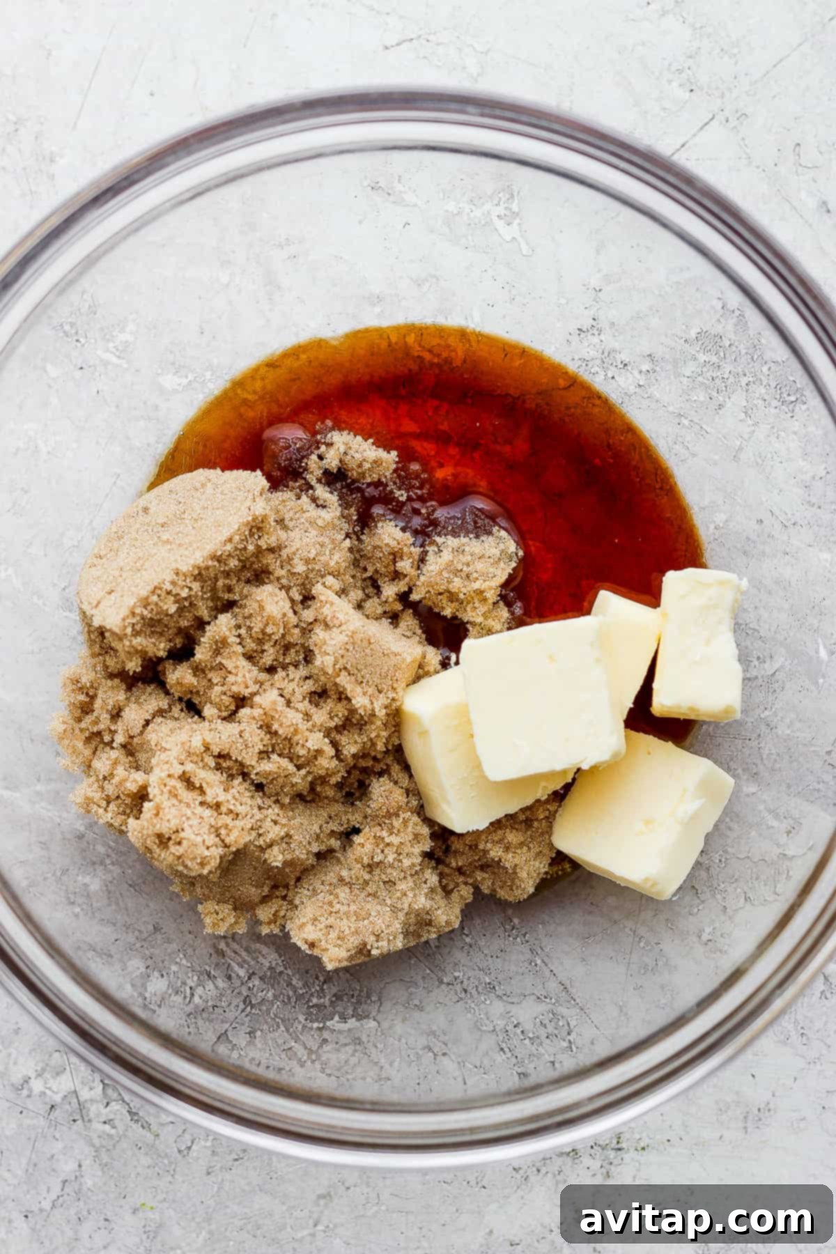 A glass bowl filled with softened unsalted butter and light brown sugar, ready for mixing.