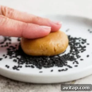 a hand is holding a cookie with sesame seeds on it.