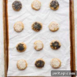 Raw tahini cookies, coated with sesame seeds, arranged on a parchment-lined baking sheet.