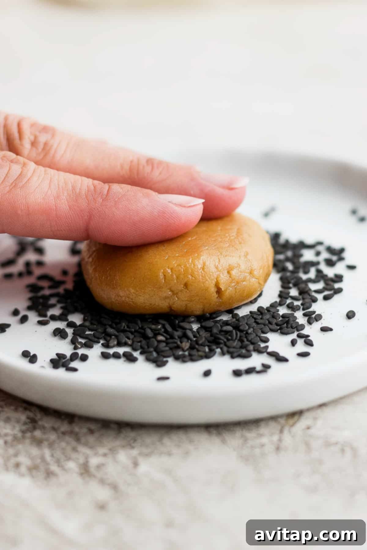 A hand gently holding a freshly baked tahini cookie, highlighting its golden exterior and sesame seed coating.