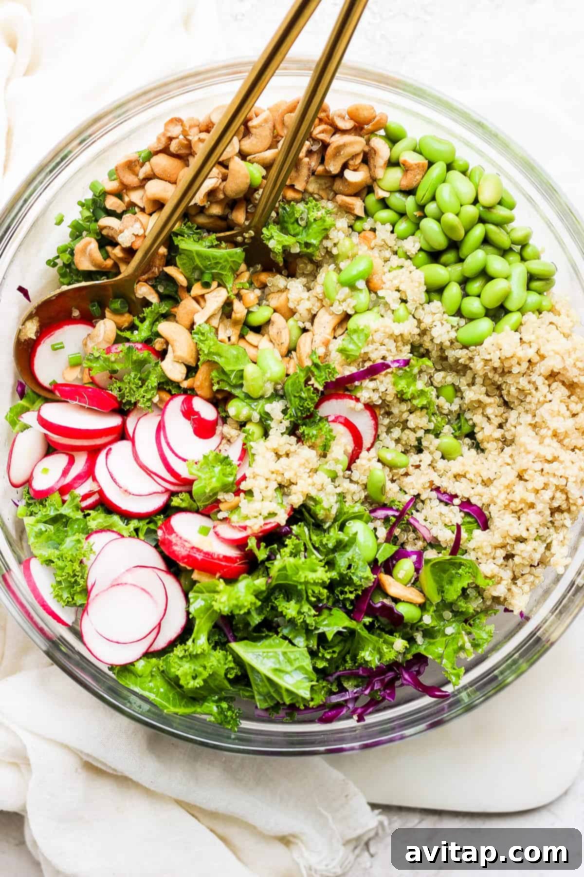 A beautifully arranged bowl of honey ginger quinoa kale salad with radishes, cashews, and a vibrant dressing.