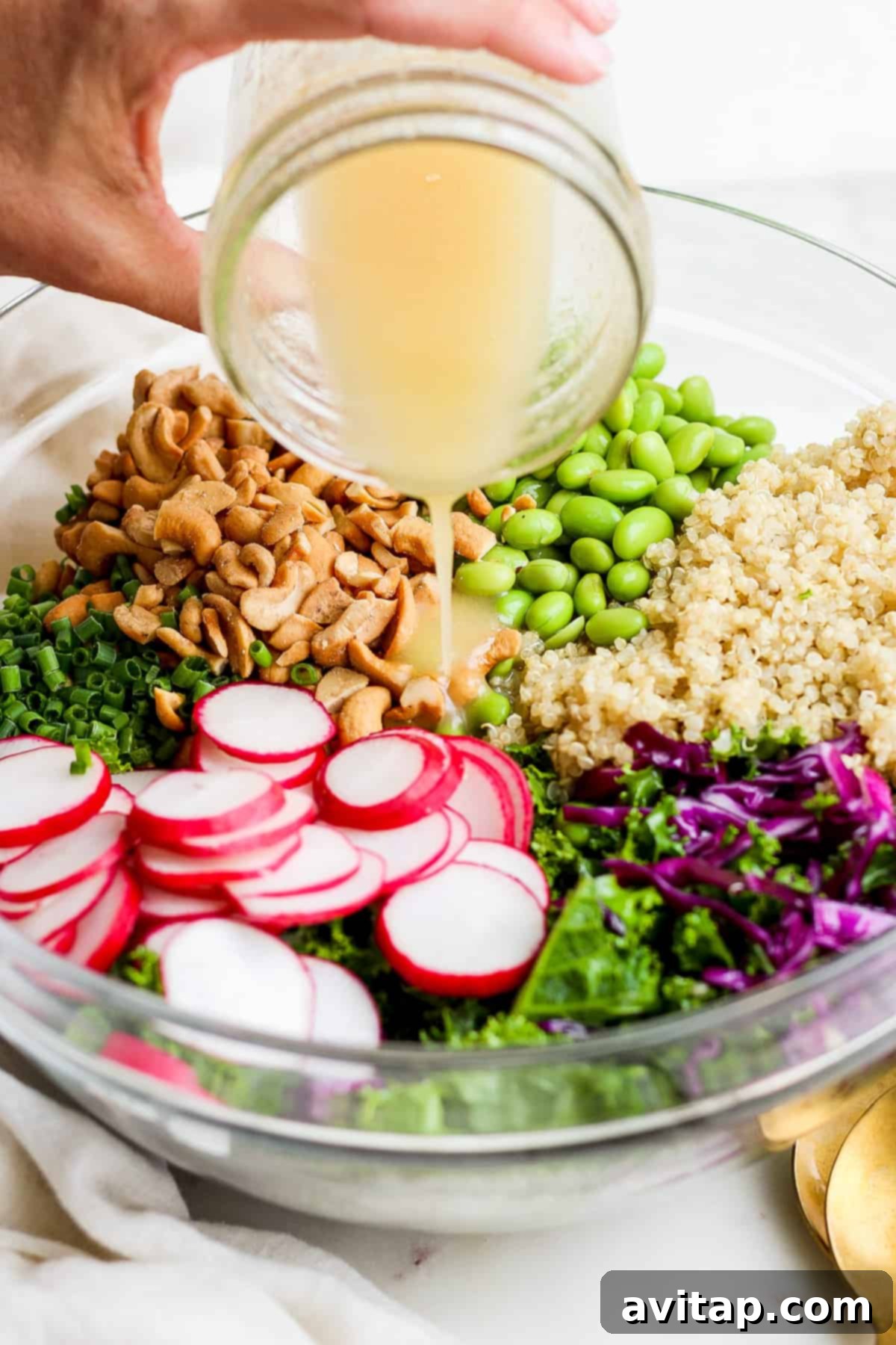 A person pouring the vibrant honey ginger dressing over a bowl of fresh greens and radishes.