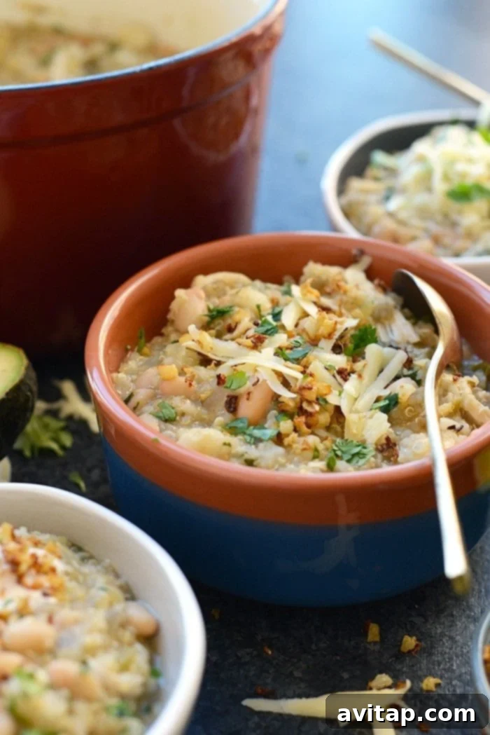 Overhead shot of a rustic wooden table featuring multiple bowls of White Chicken Quinoa Chili, each topped with a variety of fresh garnishes, ready to be served family-style.
