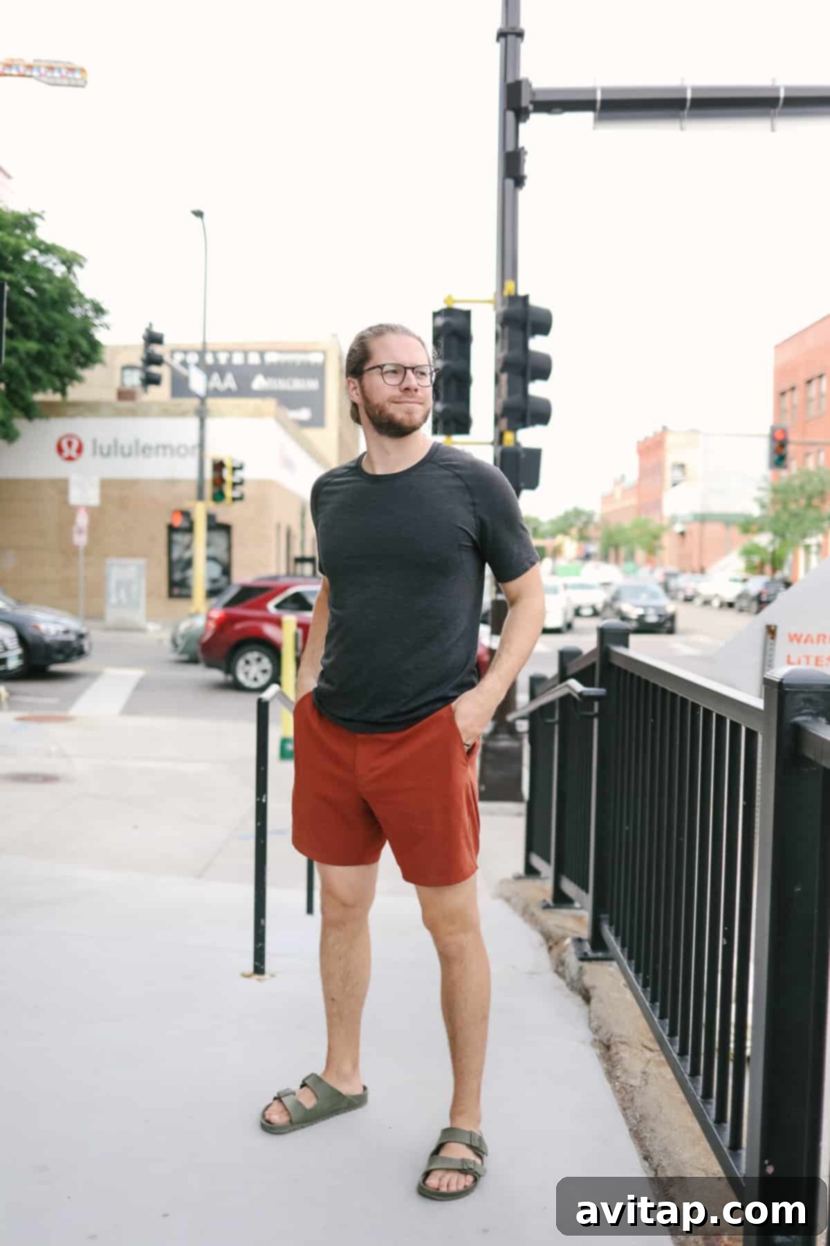 A man in Lululemon New Venture shorts standing on a sidewalk near a traffic light, highlighting urban style.