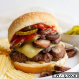 A close-up of a Mushroom Swiss burger with melted cheese and pickles on a plate.