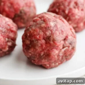 Four raw beef meatballs arranged on a white plate.