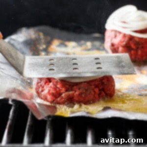 A person pressing down on burgers on a grill with a spatula.