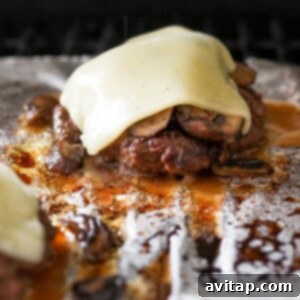 Two burgers with melted cheese and mushrooms on top of foil.