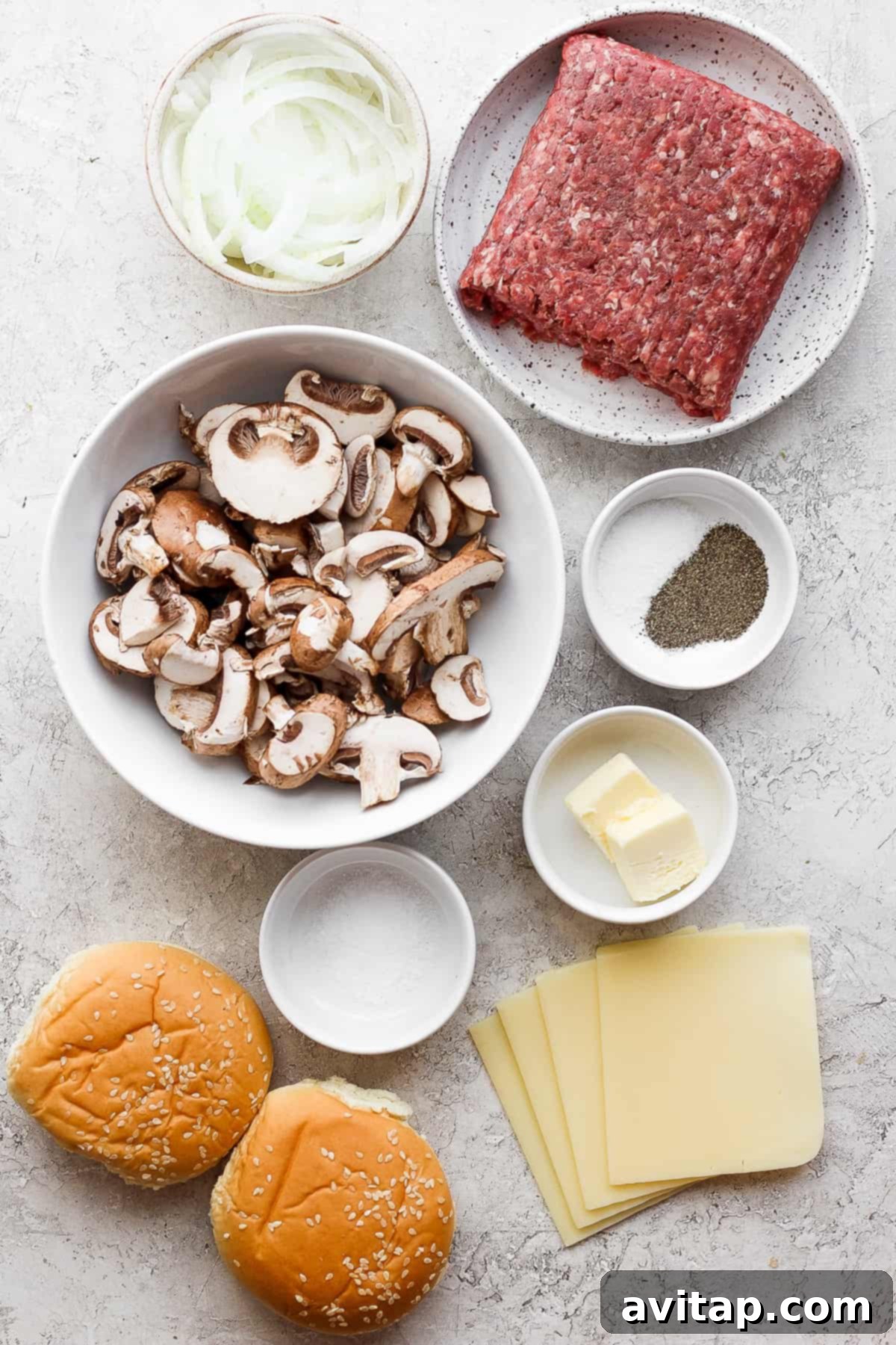 A collection of fresh ingredients laid out for a hamburger, including ground beef, sliced mushrooms, Swiss cheese, and onions.