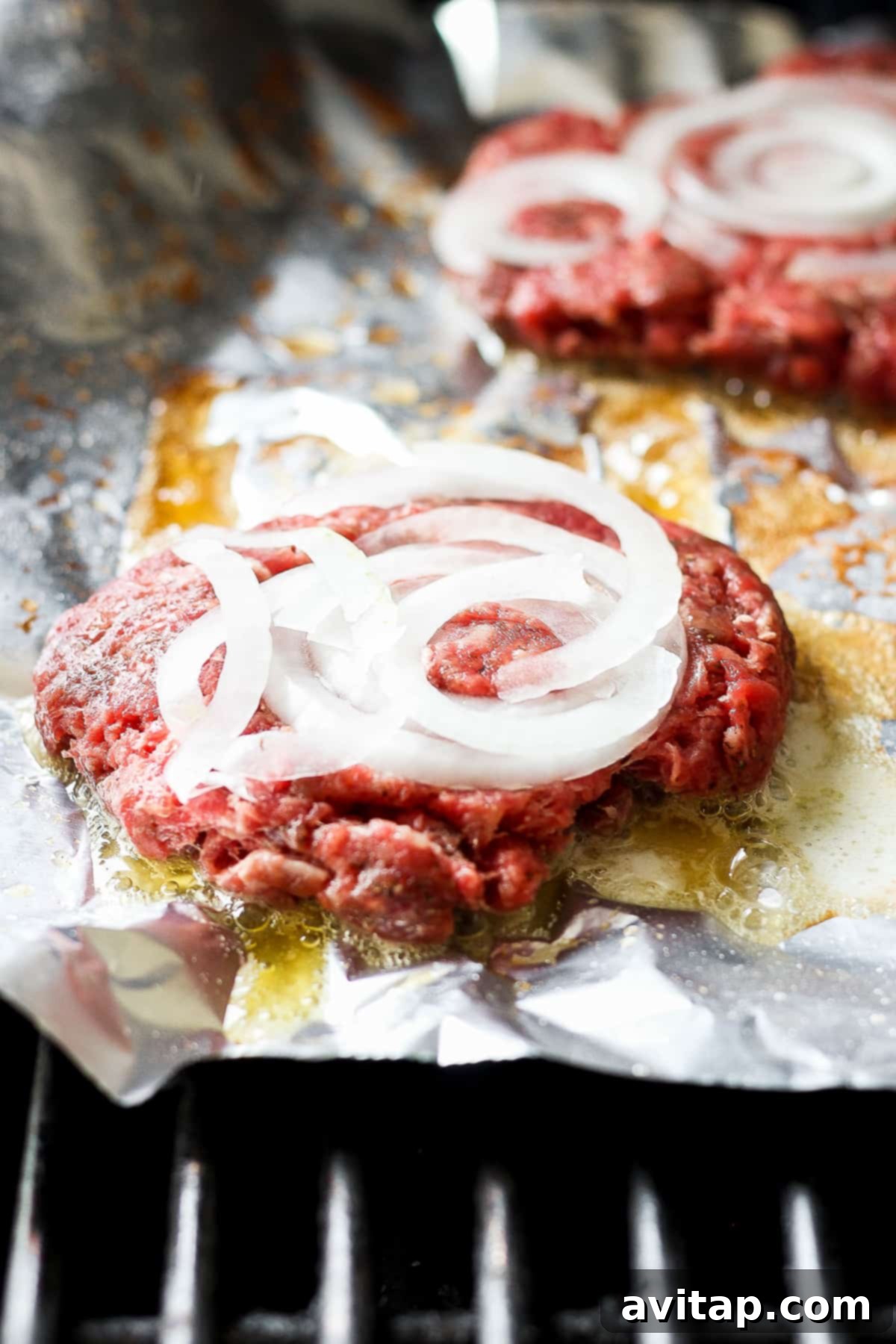 Savory Mushroom Swiss Burger 4 Raw beef burger patties topped with thinly sliced onions on aluminum foil, ready for the grill.
