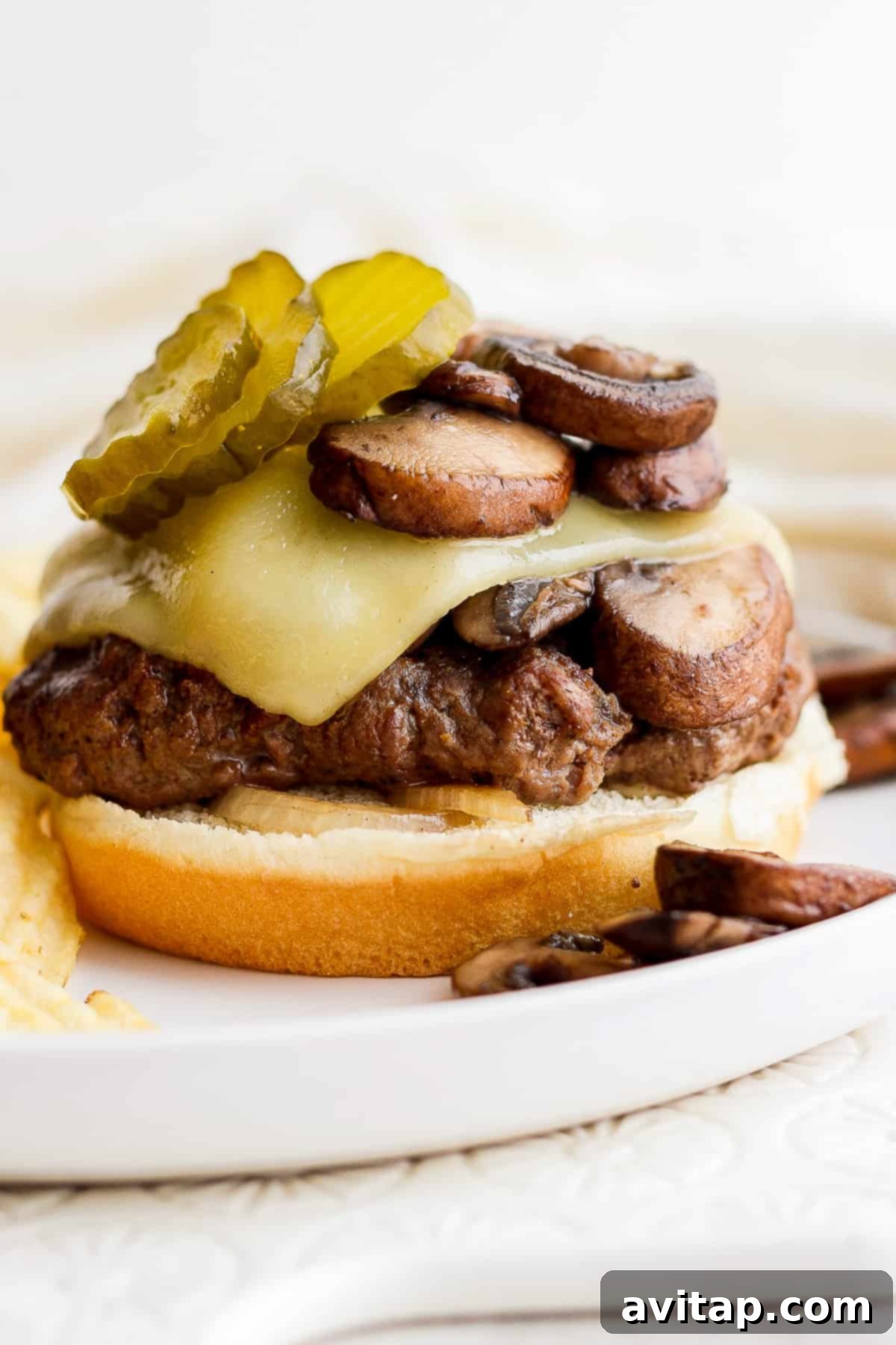 Savory Mushroom Swiss Burger 9 A delicious Mushroom Swiss burger served with pickles on a rustic plate, ready to be enjoyed.