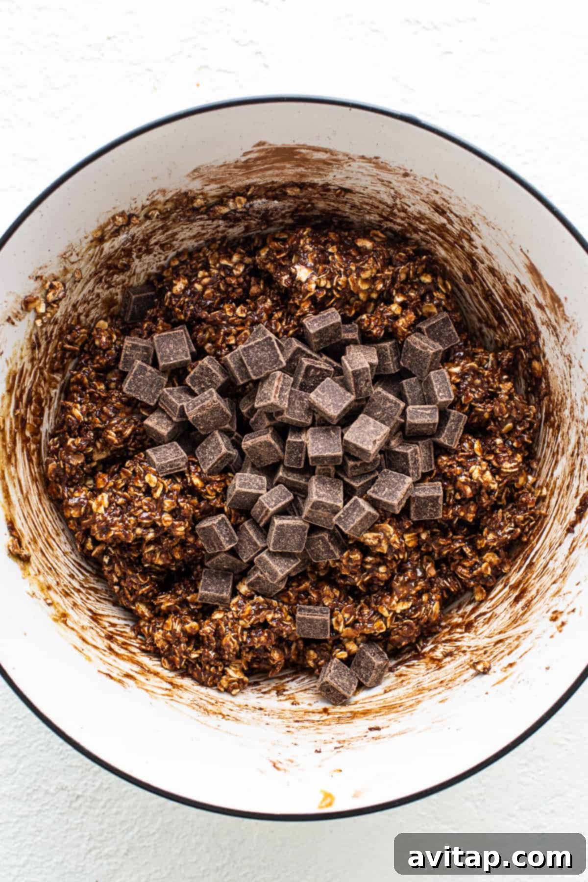 A bowl of rich chocolate oatmeal cookie dough with visible chocolate chips, ready for shaping and baking.
