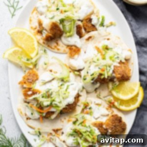 Beautifully assembled fish tacos on a white plate, complete with slaw, sauce, and lemon wedges.