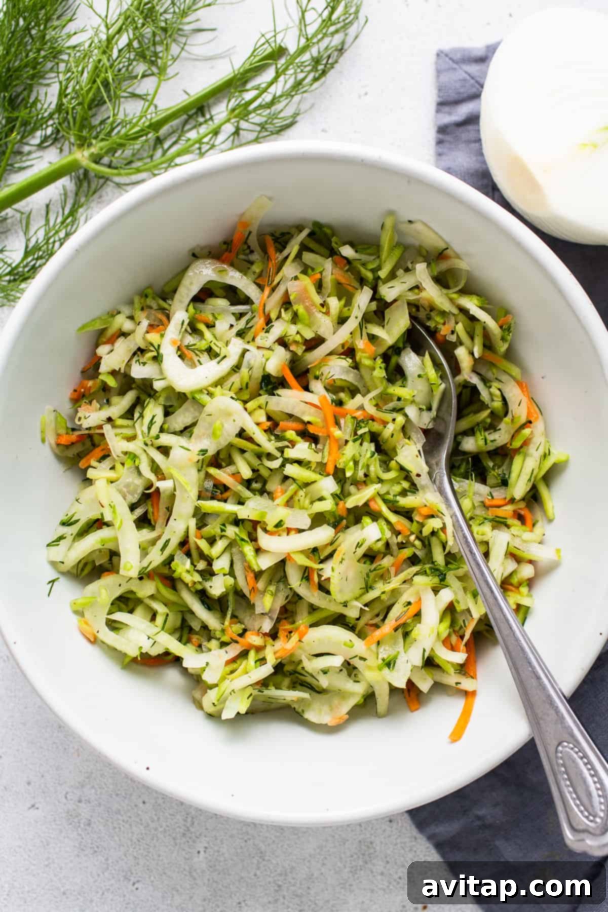 A vibrant bowl of dill coleslaw, featuring shredded carrots, white onions, and thinly sliced fennel, ready to be served.