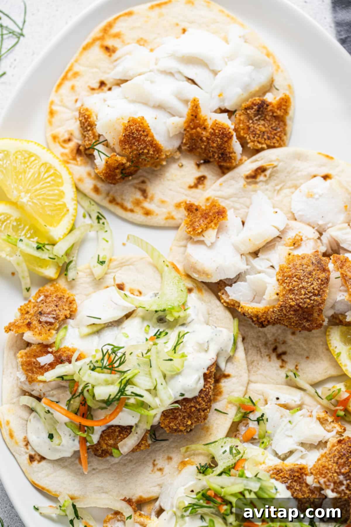 Three beautifully assembled fish tacos displayed on a white plate, garnished with fresh lemon wedges, highlighting their vibrant ingredients.