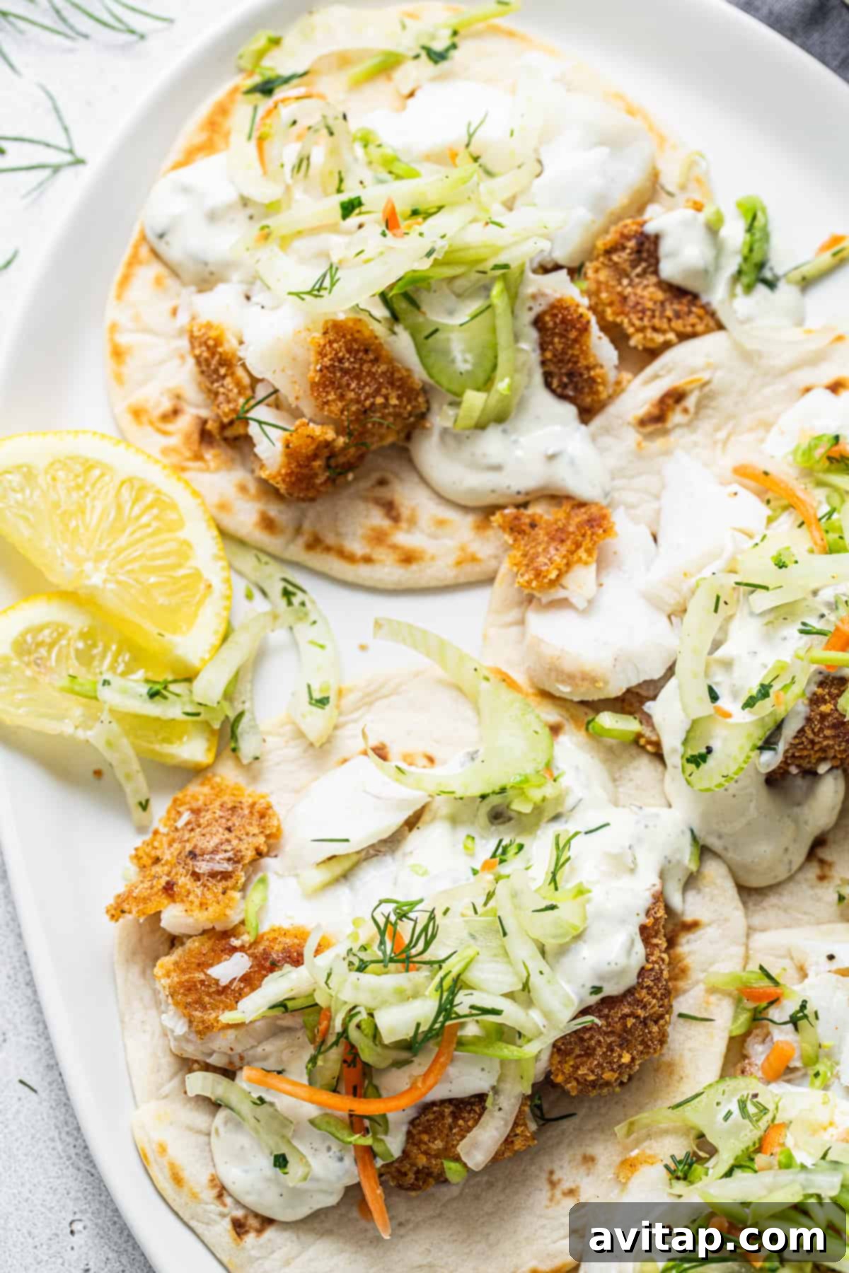 Close-up of a single fish taco, showcasing the crispy fish, colorful slaw, and a fresh lemon wedge on a pristine white plate.