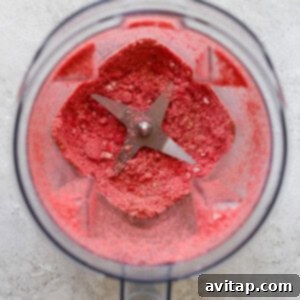 A food processor containing processed vanilla wafers and freeze-dried strawberries.
