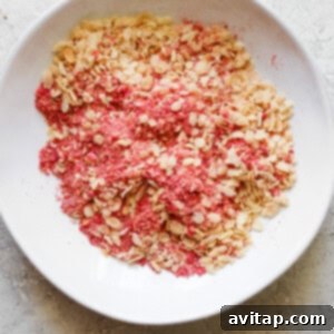 Pink granola mixture in a white bowl, ready for coating.