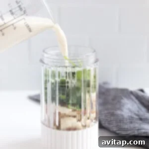 A person pouring milk into a glass pitcher as part of smoothie preparation.