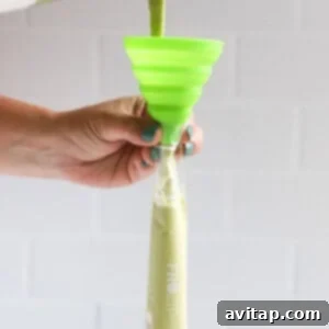 A person carefully pouring a vibrant green liquid into a plastic freeze-pop sleeve.