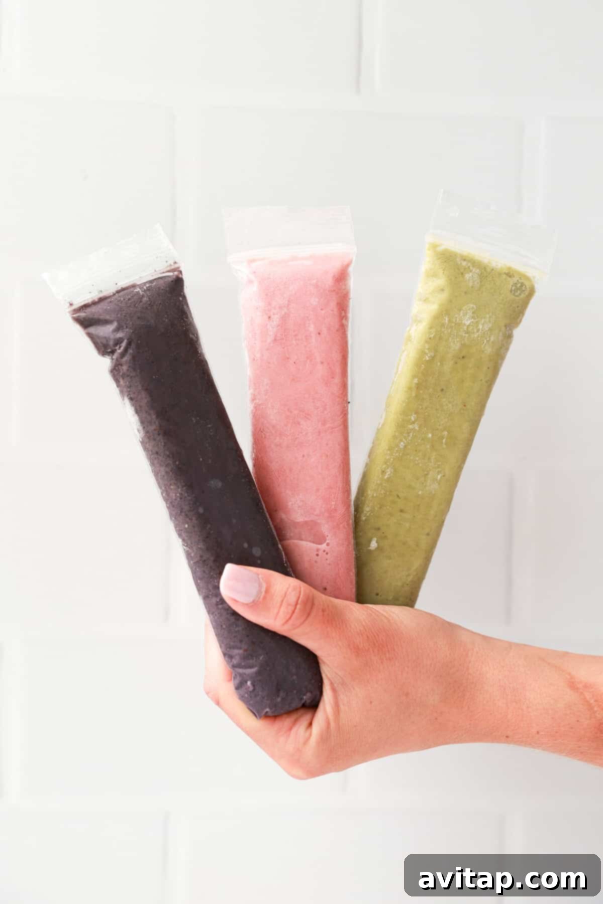 A hand holding three frozen popsicles of different flavors, showcasing variety.
