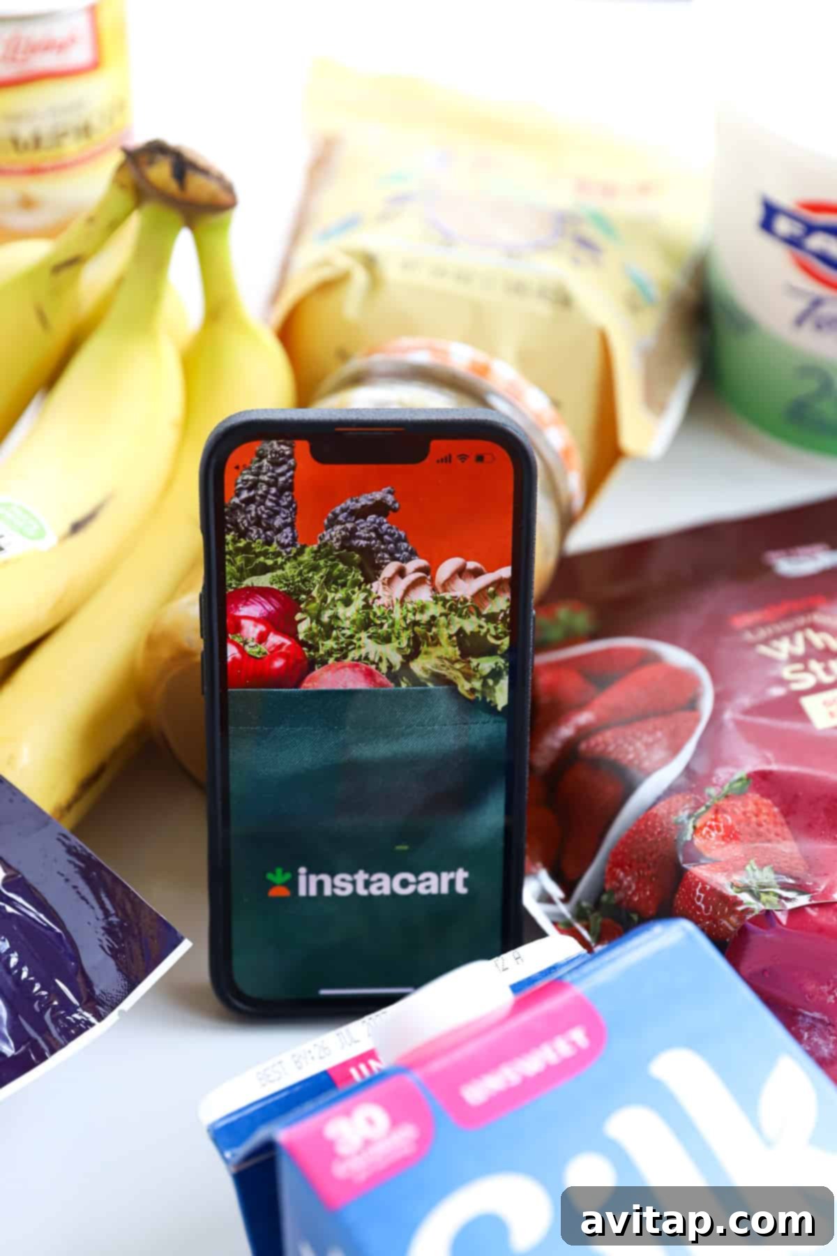 A mobile phone rests on a table next to a vibrant assortment of fresh fruits and vegetables, highlighting grocery delivery convenience.