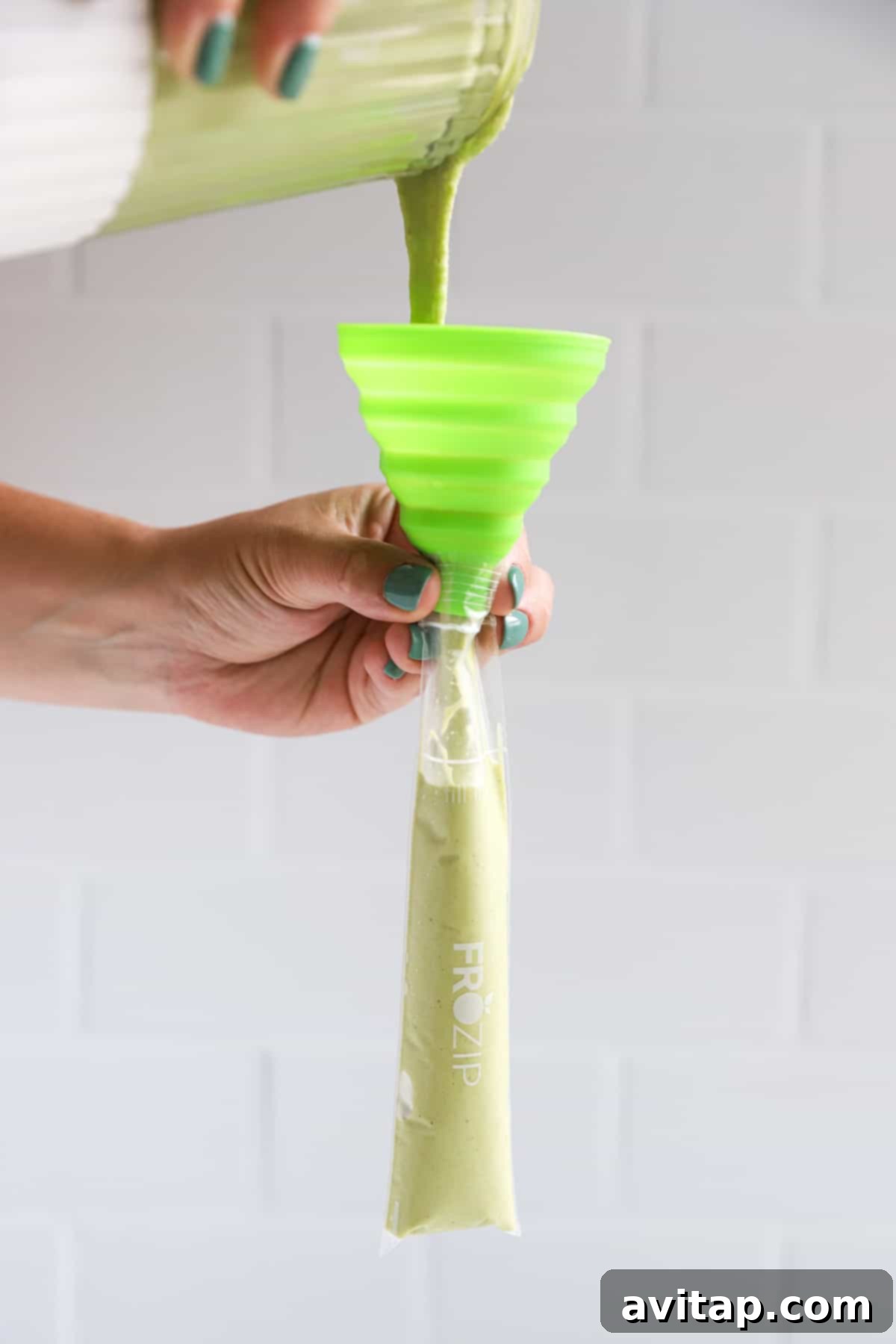 A person carefully pouring a vibrant green liquid into a plastic freeze-pop sleeve.