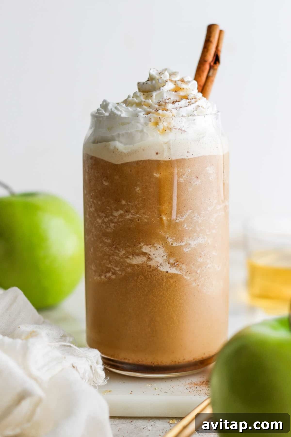 A mug filled with the Apple Crisp Oatmilk Frappuccino, topped with maple whipped cream, apple slices, and cinnamon sticks.