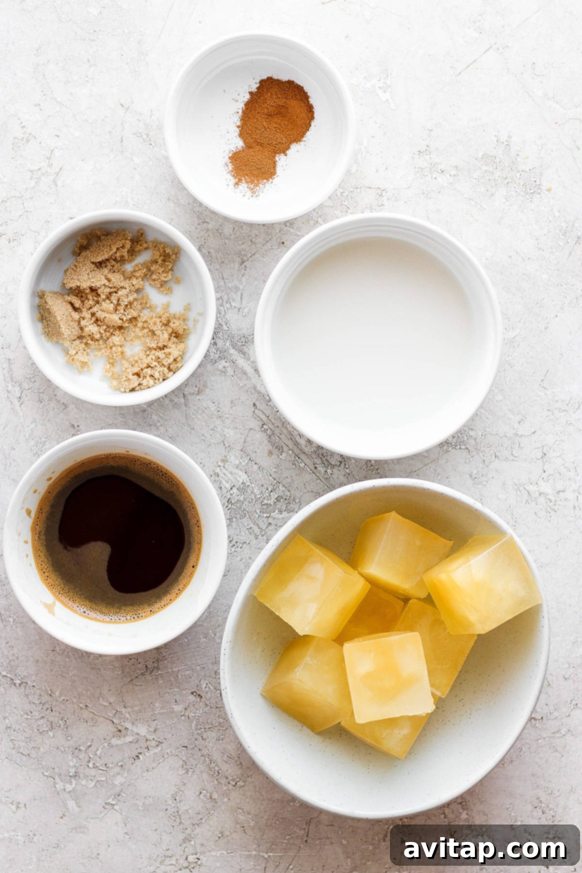 A flat lay of ingredients for a fall-themed drink, including whole apples, cinnamon sticks, brown sugar, and oat milk in bowls.
