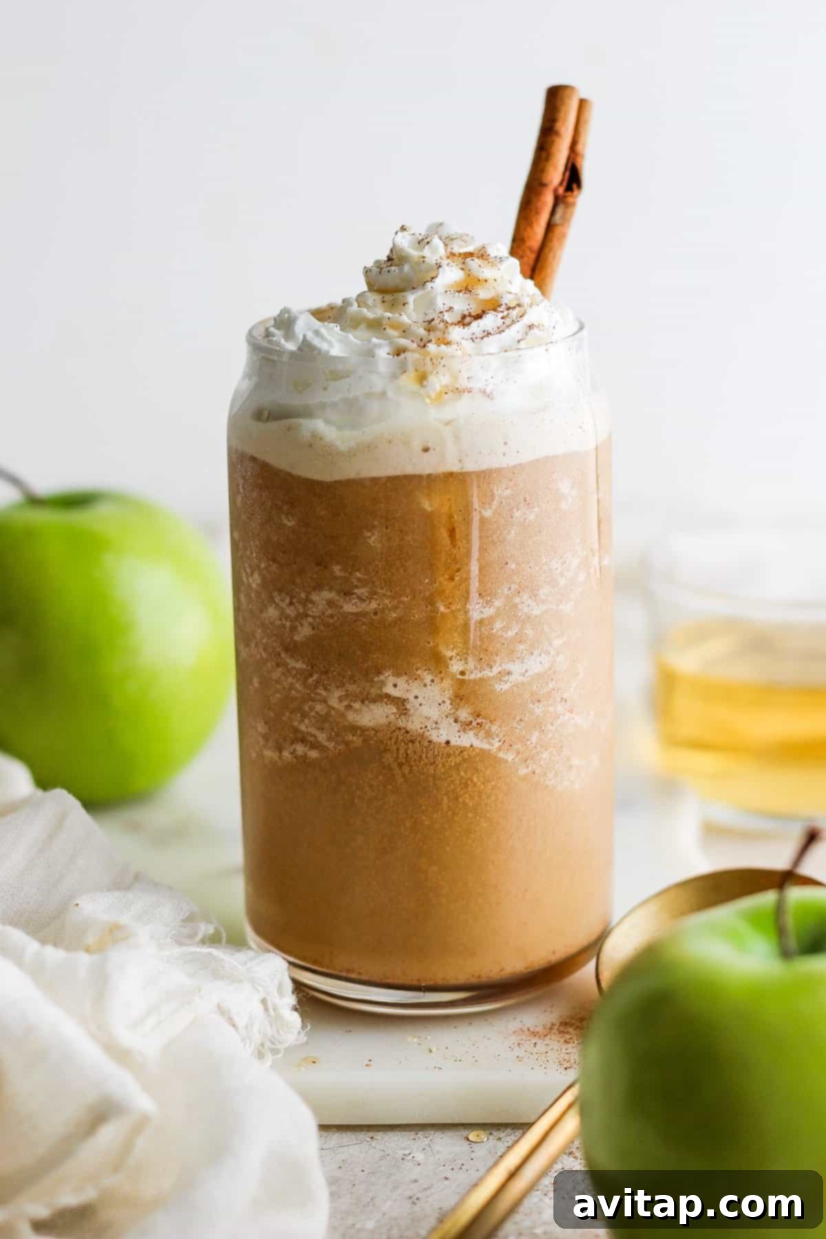 A festive pumpkin spice latte adorned with whipped cream, cinnamon stick, and fresh apple slices, set against an autumnal background.