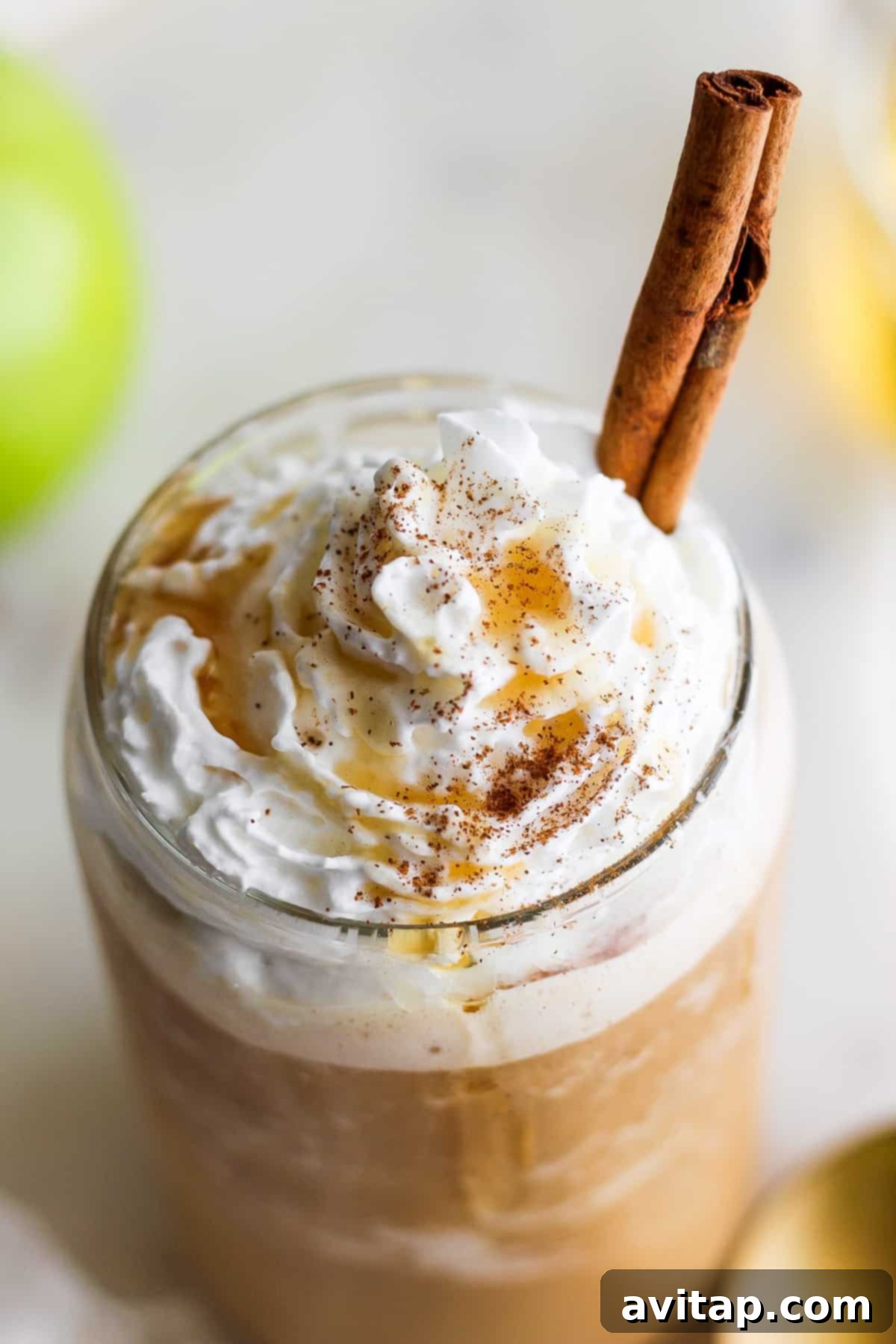 An elegantly presented apple latte with a swirl of whipped cream and a single cinnamon stick for garnish.
