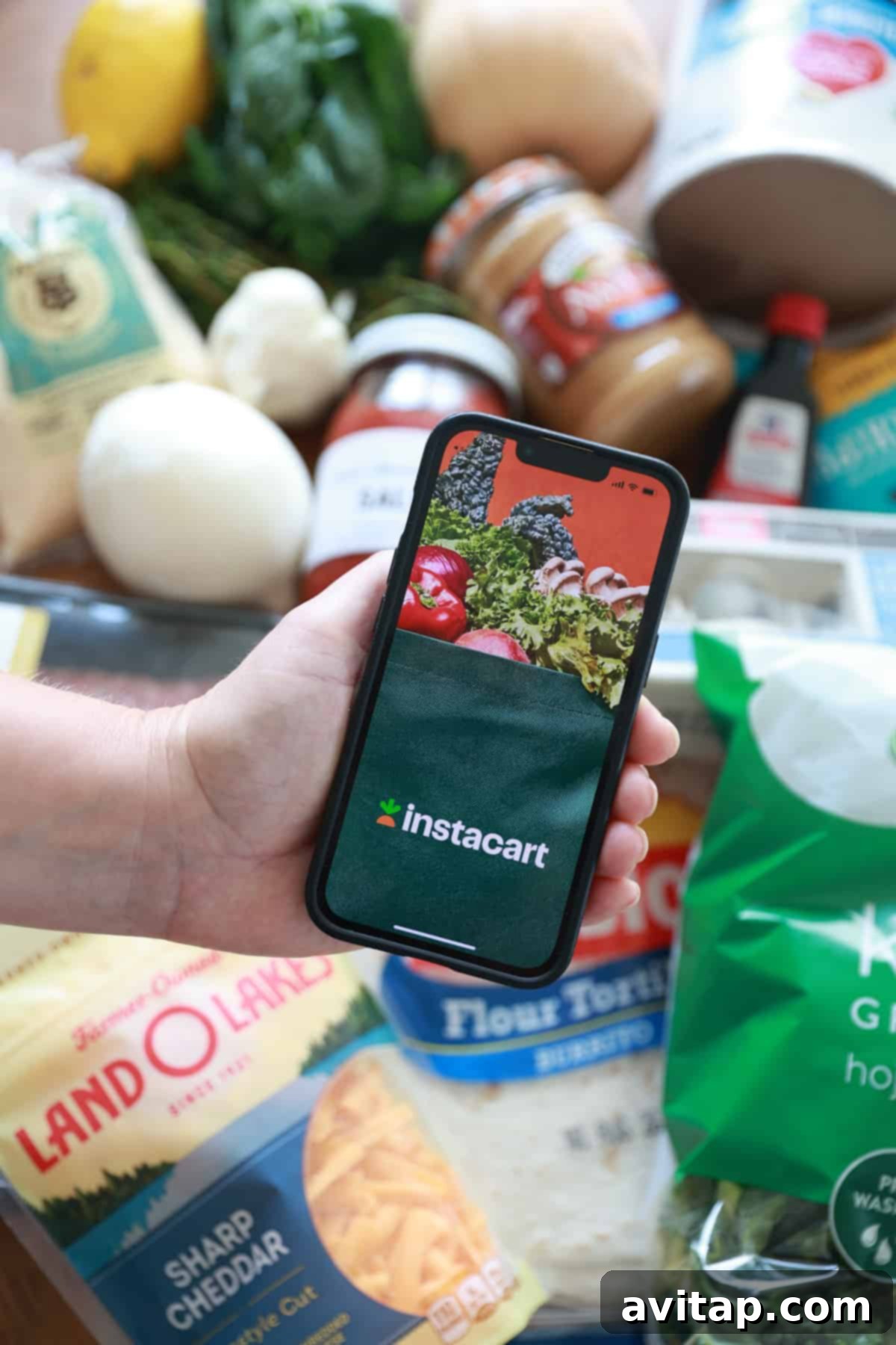 Postpartum Freezer Meal Prep Guide 3 A person using a smartphone to order groceries via Instacart, with fresh produce and groceries visible in the background.