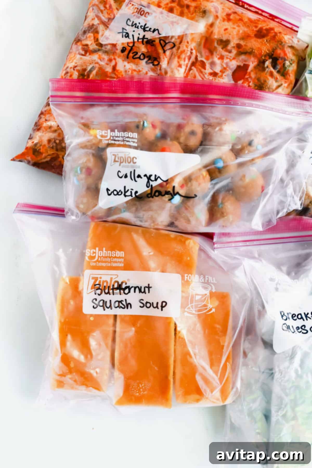 Postpartum Freezer Meal Prep Guide 4 A vibrant assortment of prepared freezer meals, including chicken fajitas and breakfast quesadillas, in labeled plastic bags on a clean white surface.