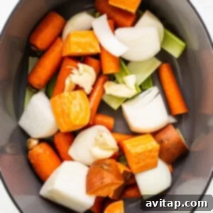 A large cooking pan filled with fresh, coarsely chopped carrots, onions, and celery, ready for the initial simmering process to create a flavorful base.