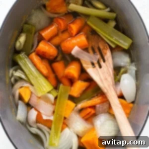 A large pot filled with carrots, celery, and onions, simmering gently on a stovetop, indicating the slow cooking process for developing rich flavors.