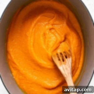 A wooden spoon stirring a pot of bright orange, smooth pureed vegetable sauce, showcasing its creamy and even texture.