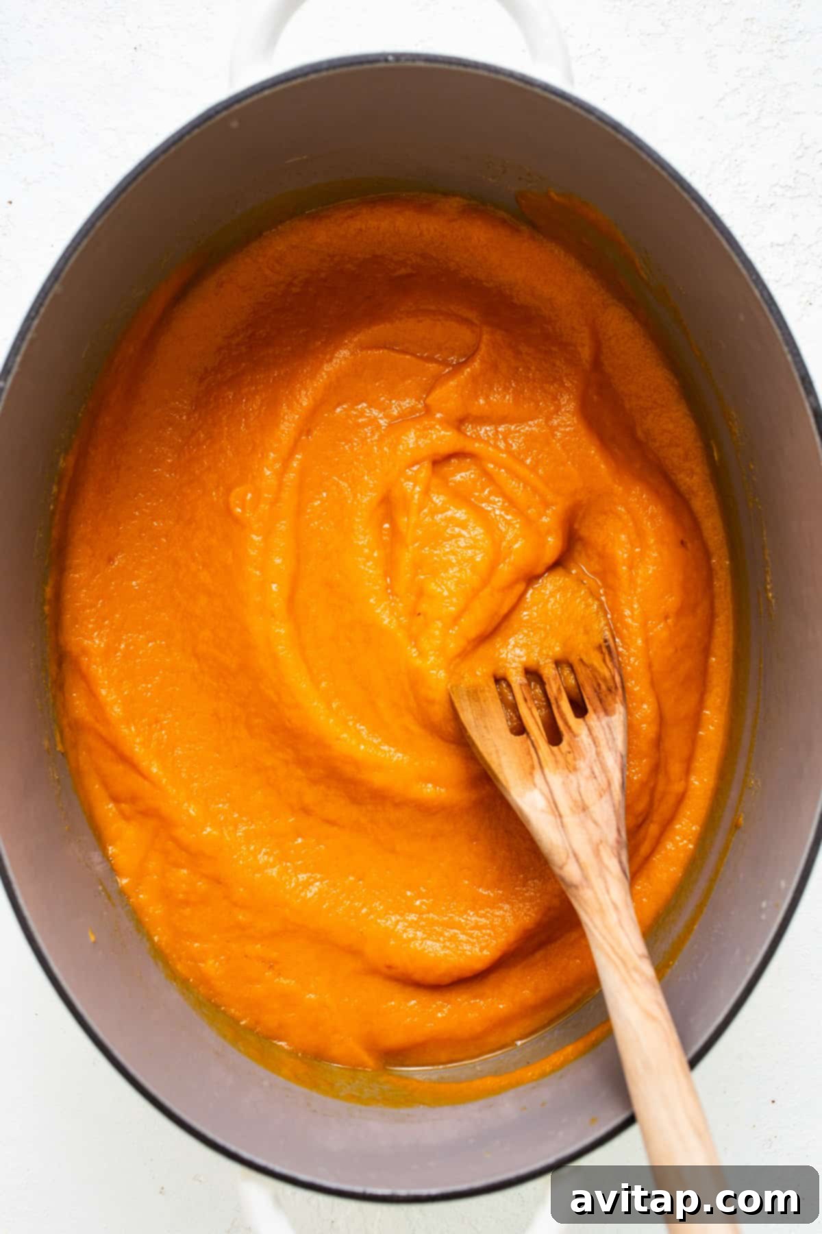 One-Pot Hidden Veggie O's 4 A sturdy wooden spoon resting in a large pot of thick, vibrant orange-hued vegetable puree, glistening and ready for the pasta, showcasing the smooth, rich texture of the sauce base.