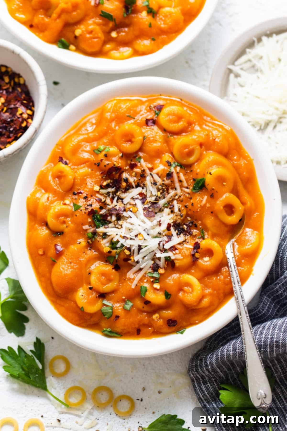 One-Pot Hidden Veggie O's 6 Two aesthetically pleasing bowls of creamy, orange pasta, generously garnished with fresh herbs and a sprinkle of cheese, placed on a light wooden table, perfectly ready to be savored.