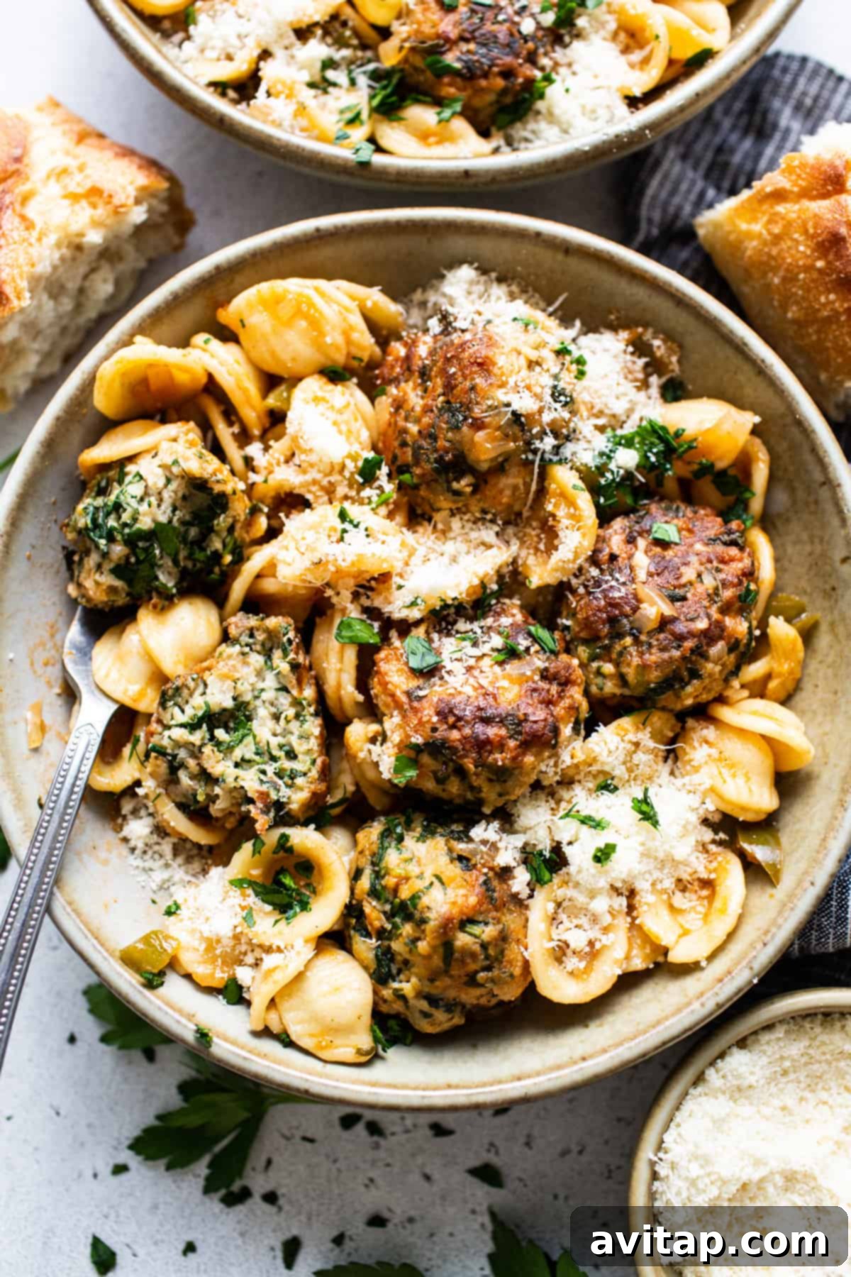 A bowl of pasta with meatballs and parmesan.