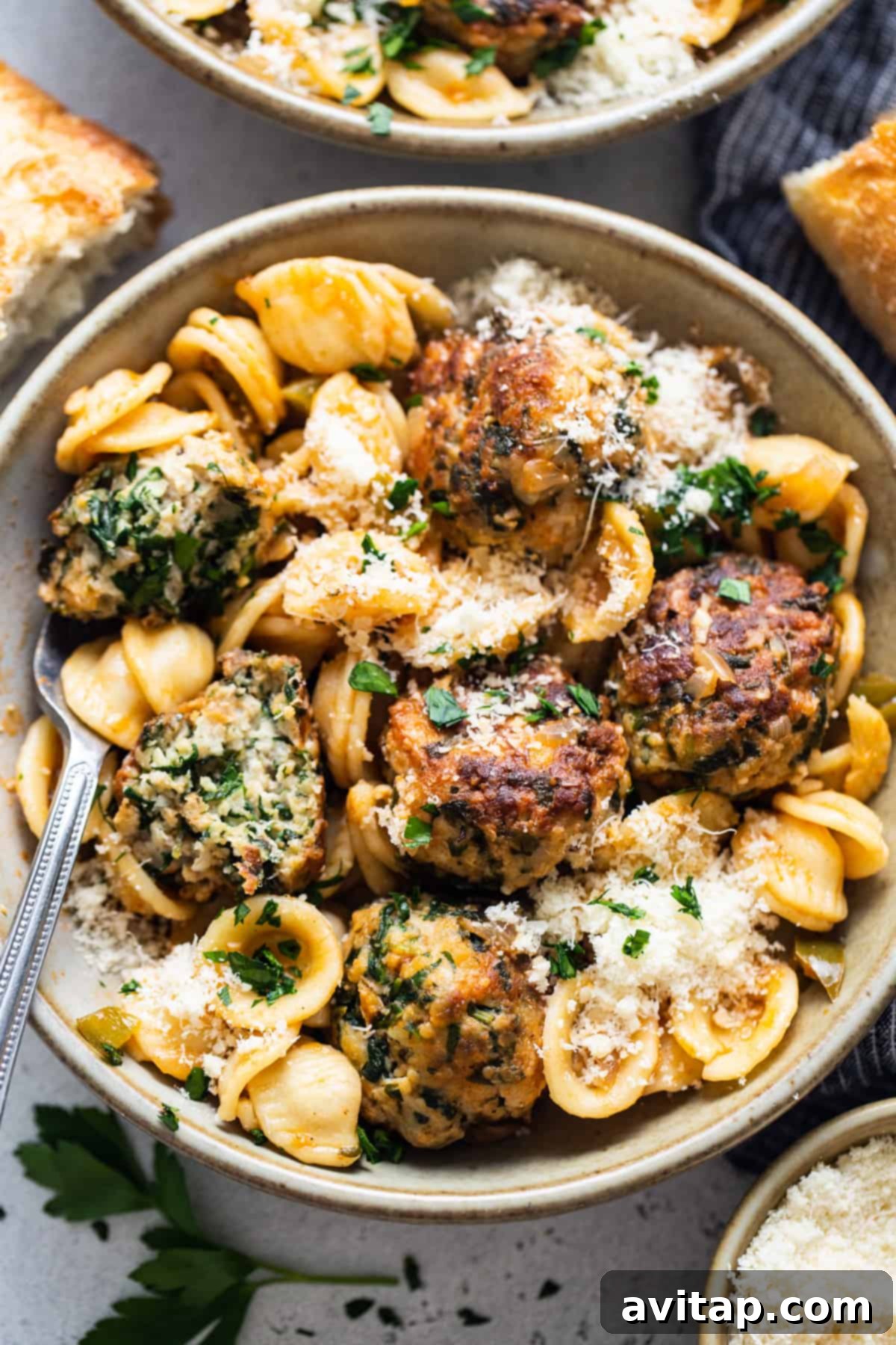A bowl of pasta with meatballs and parmesan.