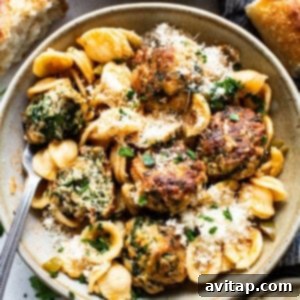 A bowl of pasta with meatballs and spinach.