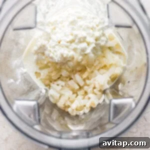 A food processor blending cottage cheese with sautéed garlic and onion into a smooth, creamy Alfredo sauce.