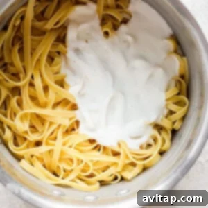 A pot of fettuccine pasta being coated in a rich, creamy cottage cheese Alfredo sauce.