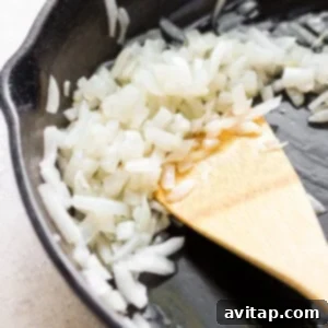 A frying pan with sautéed onions and garlic, stirred with a wooden spoon, for the Alfredo sauce.