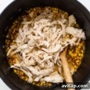 Shredded chicken and corn in a pan, stirred into the chili base, ready for the final touches.