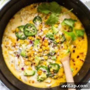 Creamy chicken and corn chili in a pan with a wooden spoon, showing the final consistency after adding Greek yogurt.