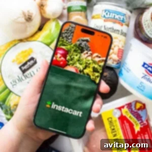 A person holding a smartphone displaying the Instacart app, with bags of groceries in the background.